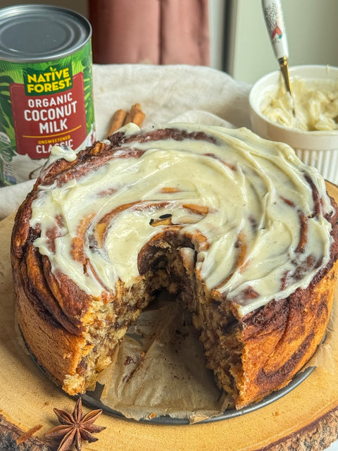 Vegan Cinnamon Roll Cake made with Native Forest Organic Coconut Milk, topped with creamy dairy-free frosting and served on a wooden board.